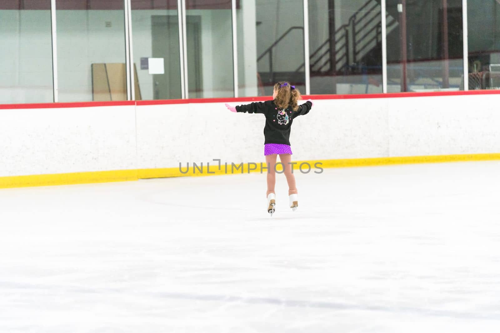 Little girl practicing figure skating on an indoor ice skating rink.