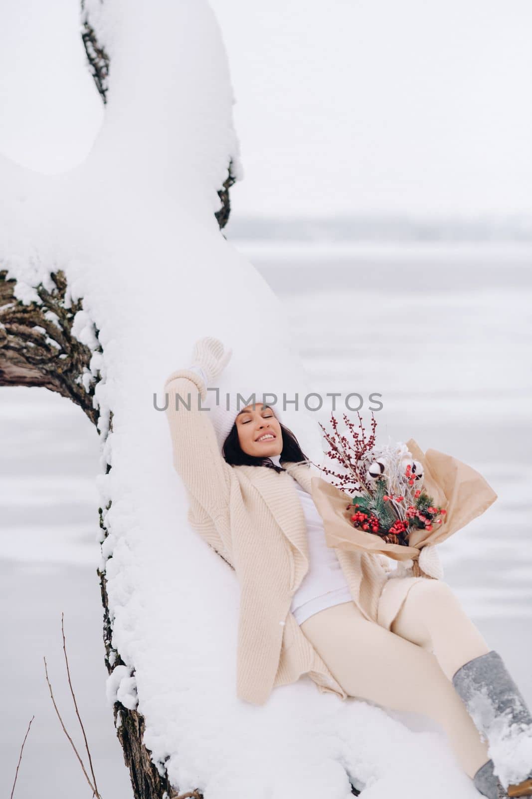 A beautiful girl in a beige cardigan and a white hat with flowers enjoys a snowy winter in nature.