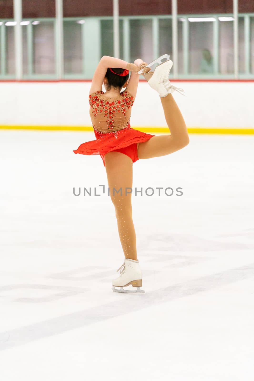 Teenage girl practicing figure skating on an indoor ice skating rink.