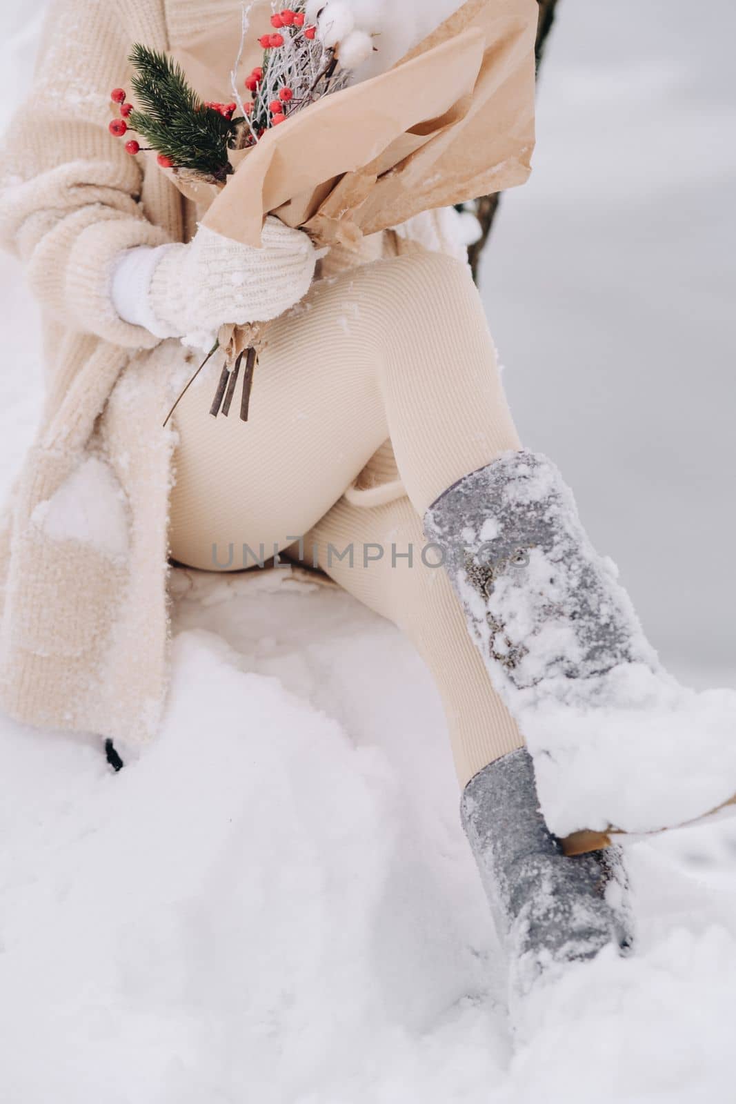 A close-up of the legs of a girl in felt boots with winter flowers sitting in nature in the snowy season. Winter weather by Lobachad