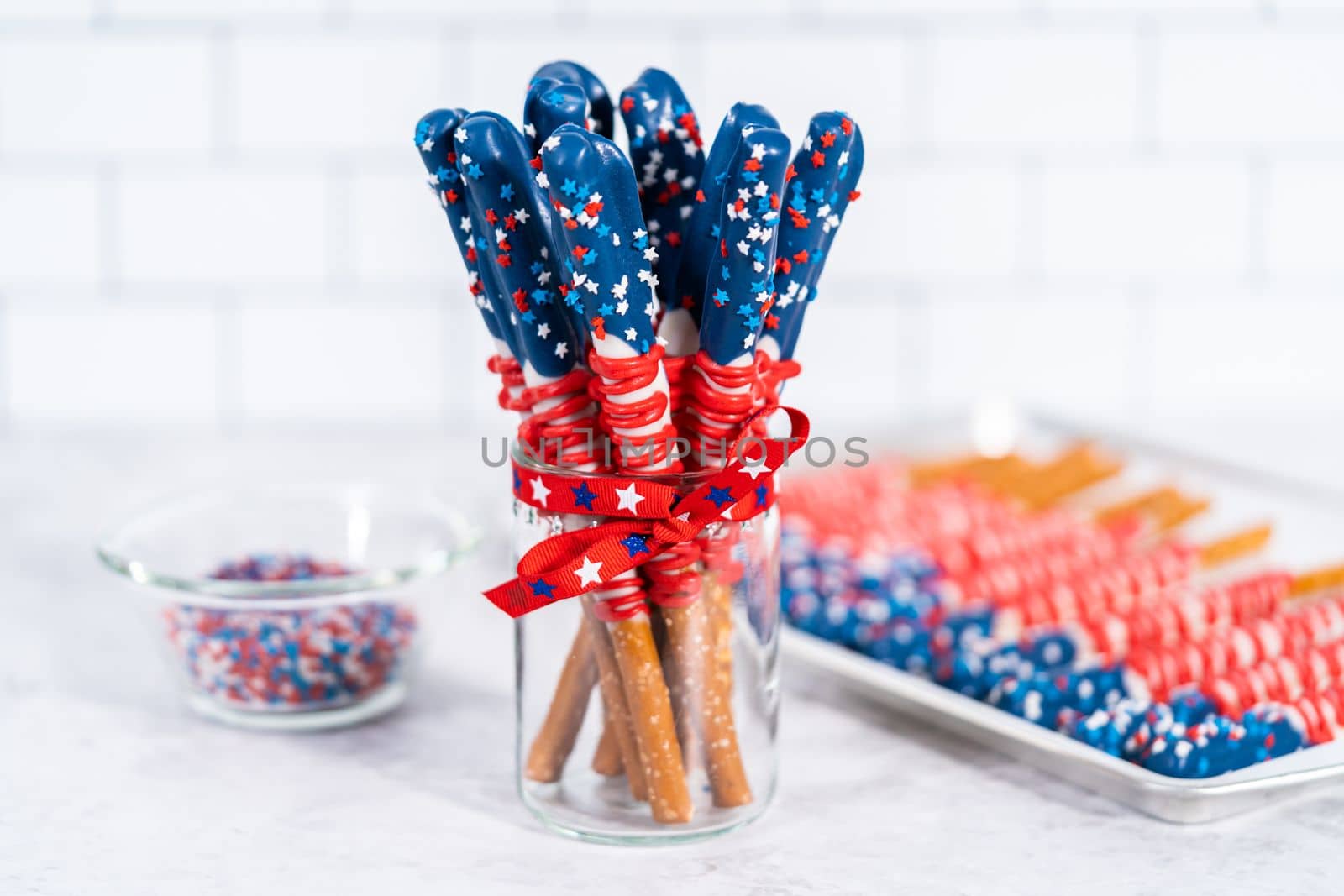 Homemade chocolate-covered pretzel rods decorated like the American flag in a glass jar.