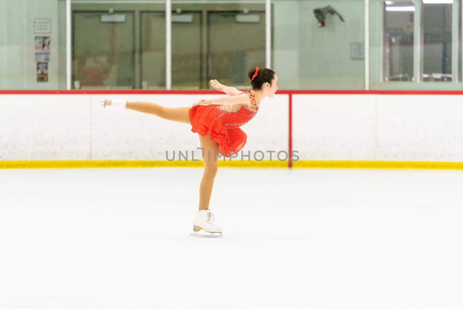 Teenage girl practicing figure skating on an indoor ice skating rink.