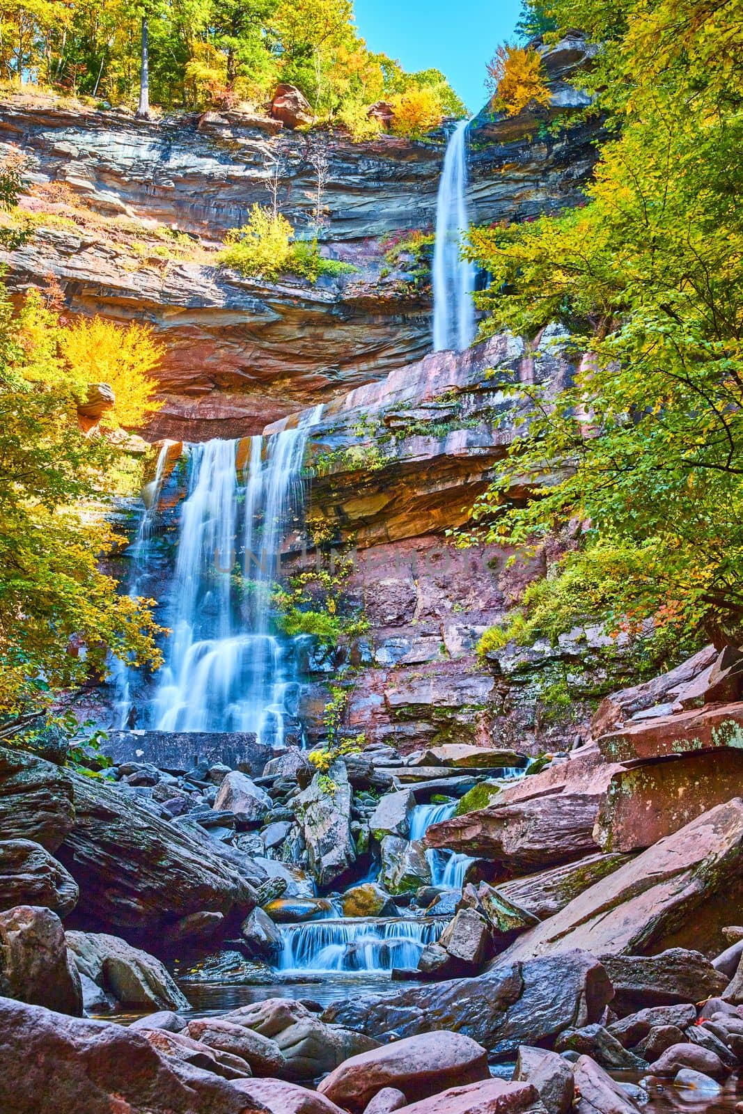 Image of Magical stunning three tiered waterfalls from below pouring over layers of cliffs in peak New York fall foliage