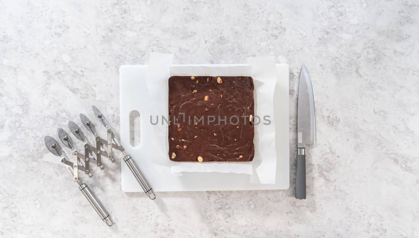 Flat lay. Removing chocolate macadamia fudge from a square cheesecake pan lined with parchment.