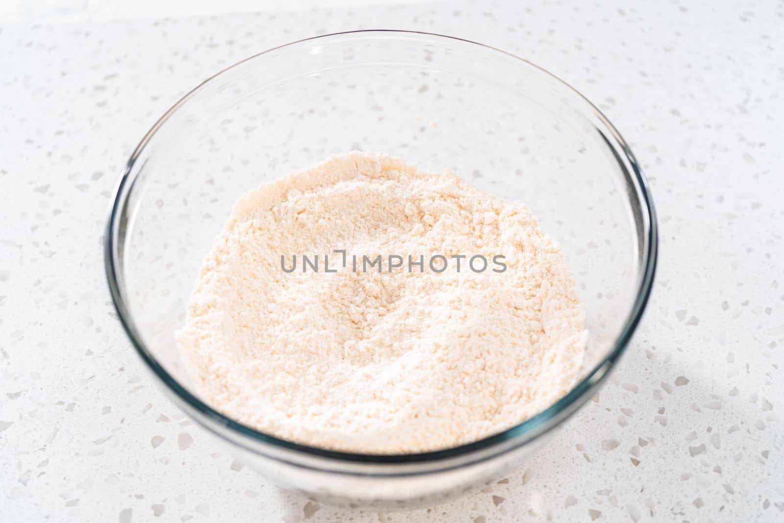 Mixing dry ingredients with a hand whisk in a large glass mixing bowl to bake a simple vanilla bundt cake.