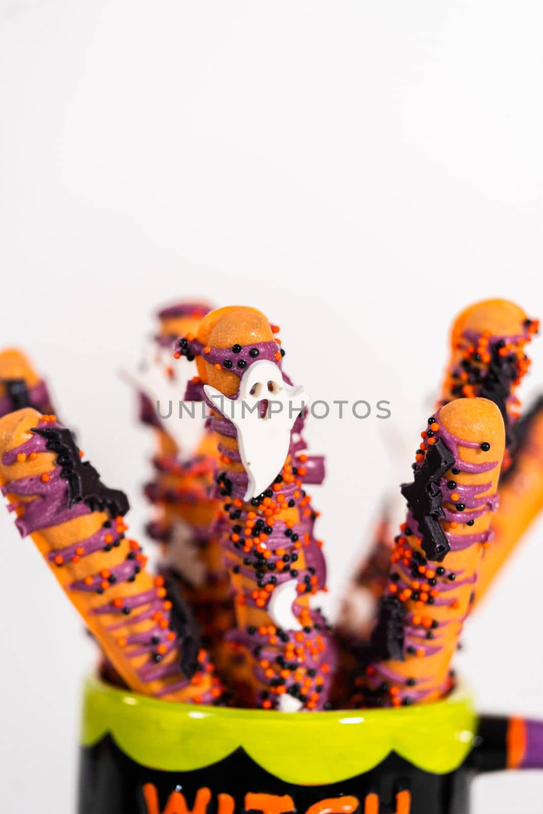 Halloween chocolate-covered pretzel rods with sprinkles in a cup.