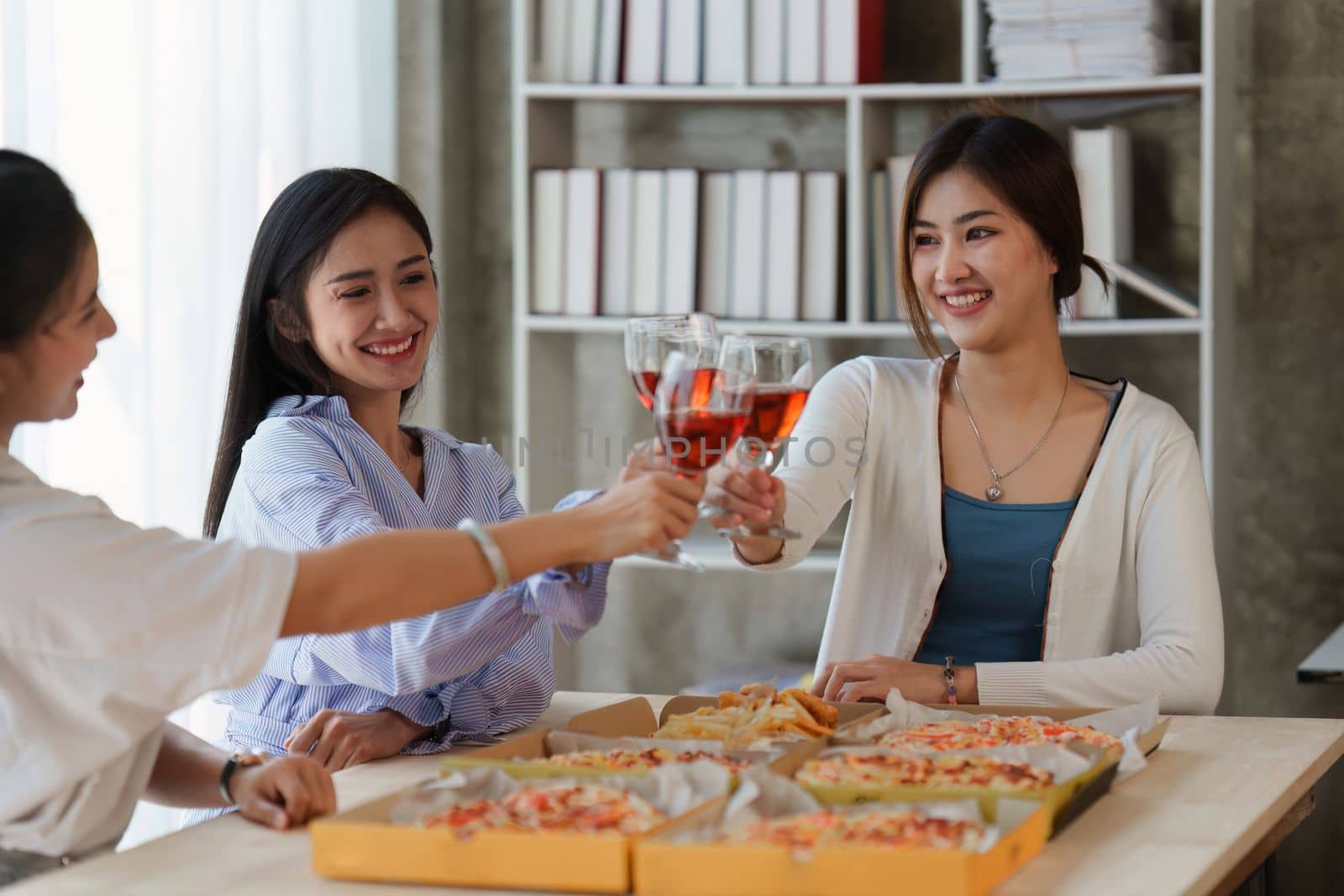 Friends at birthday party clinking glasses with champagne and pizza, enjoying Christmas vacation, pizza on the table. Holiday Party event.