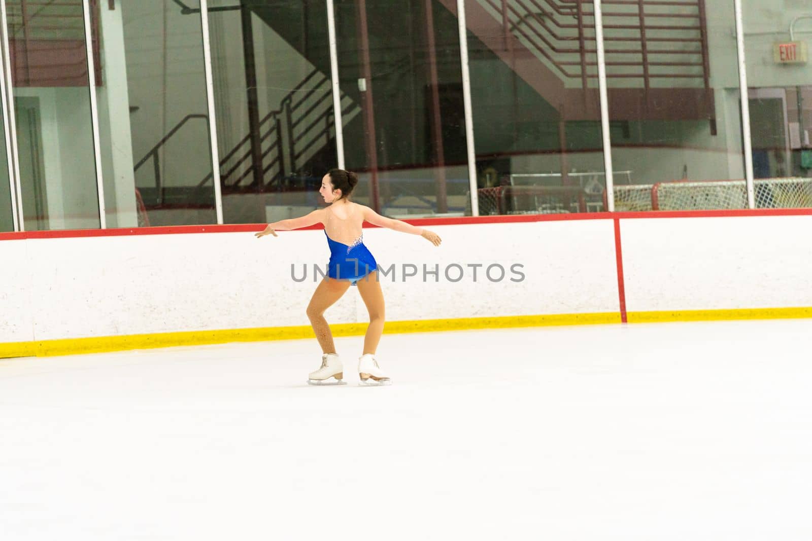 Teenage girl practicing figure skating on an indoor ice skating rink.