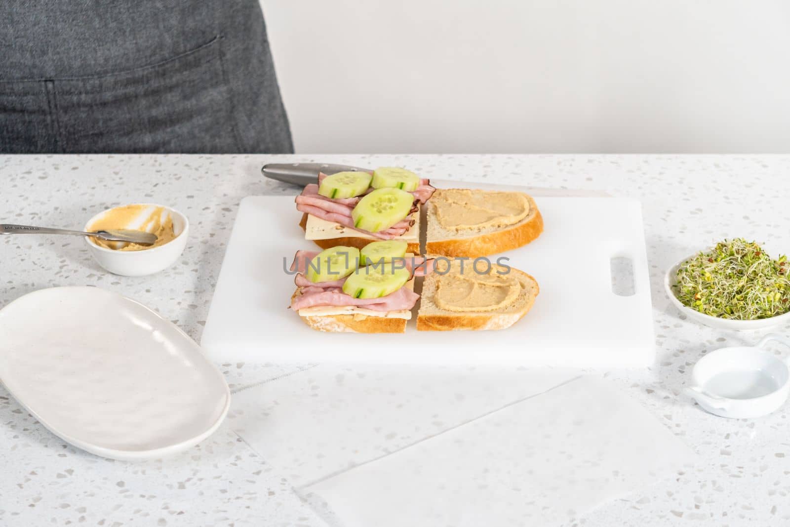 Assembling ham, cucumber, and sprout sandwiches on the white cutting board.