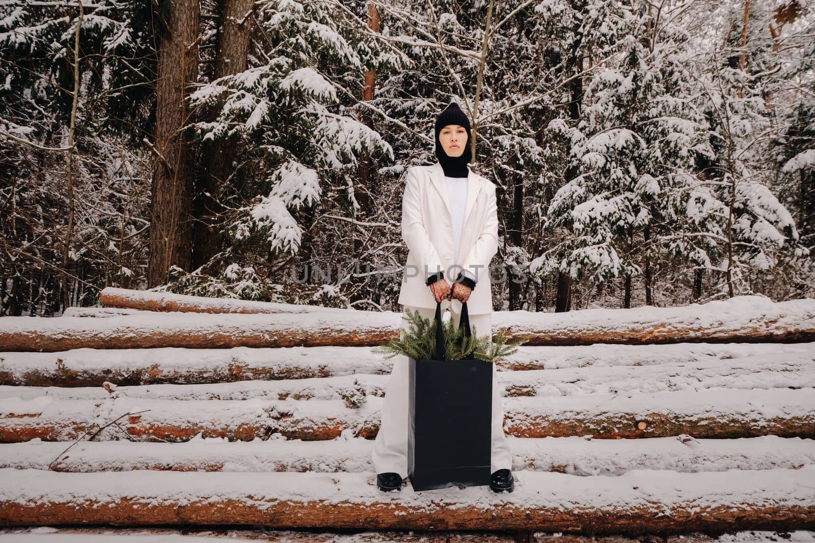 A girl in a white suit and balaclava with a package of Christmas trees in the winter forest on New Year's Eve.New Year's concept by Lobachad