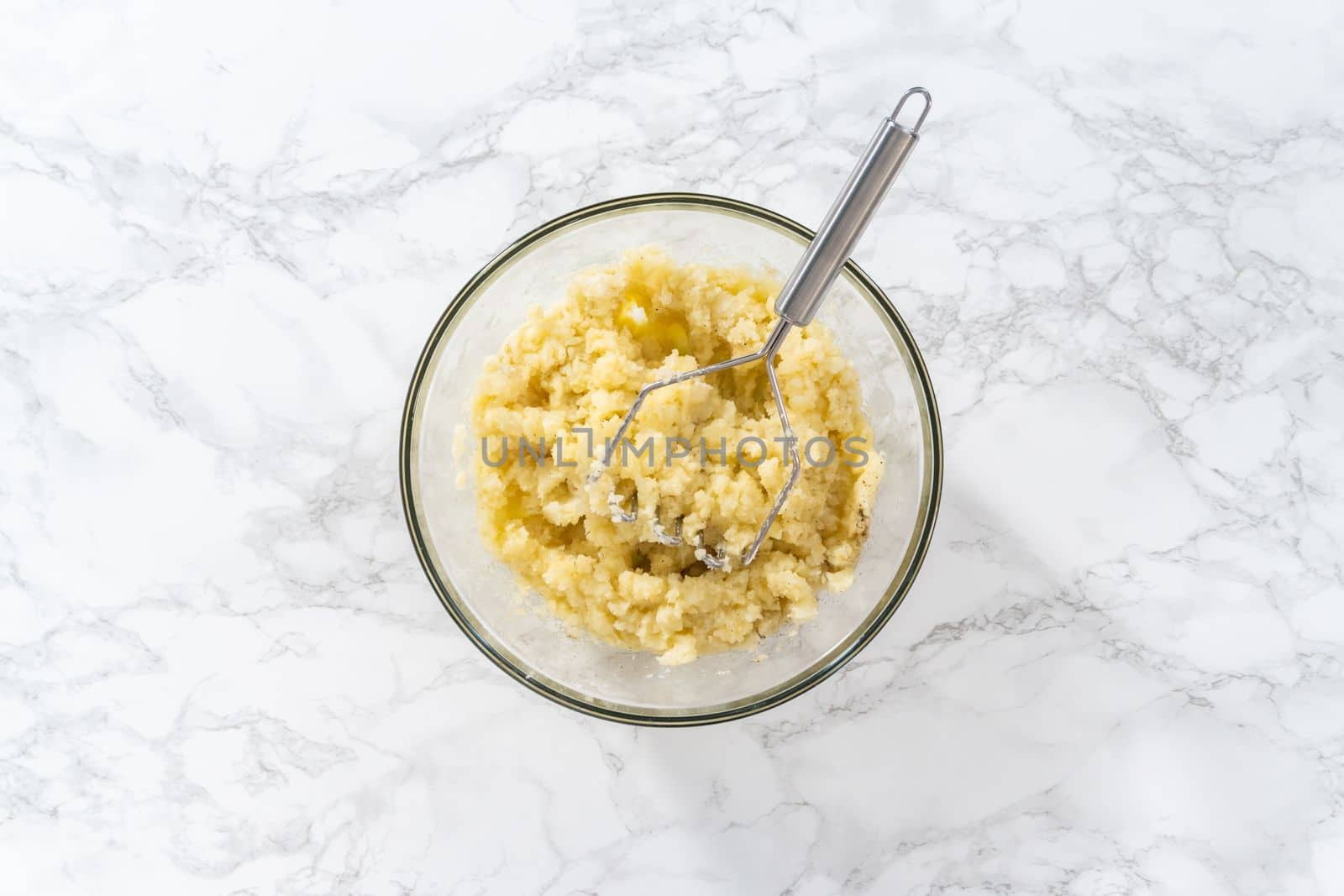 Flat lay. Mashed potatoes. Mashing cooked potatoes in a glass mixing bowl with a potato masher to make mashed potatoes.