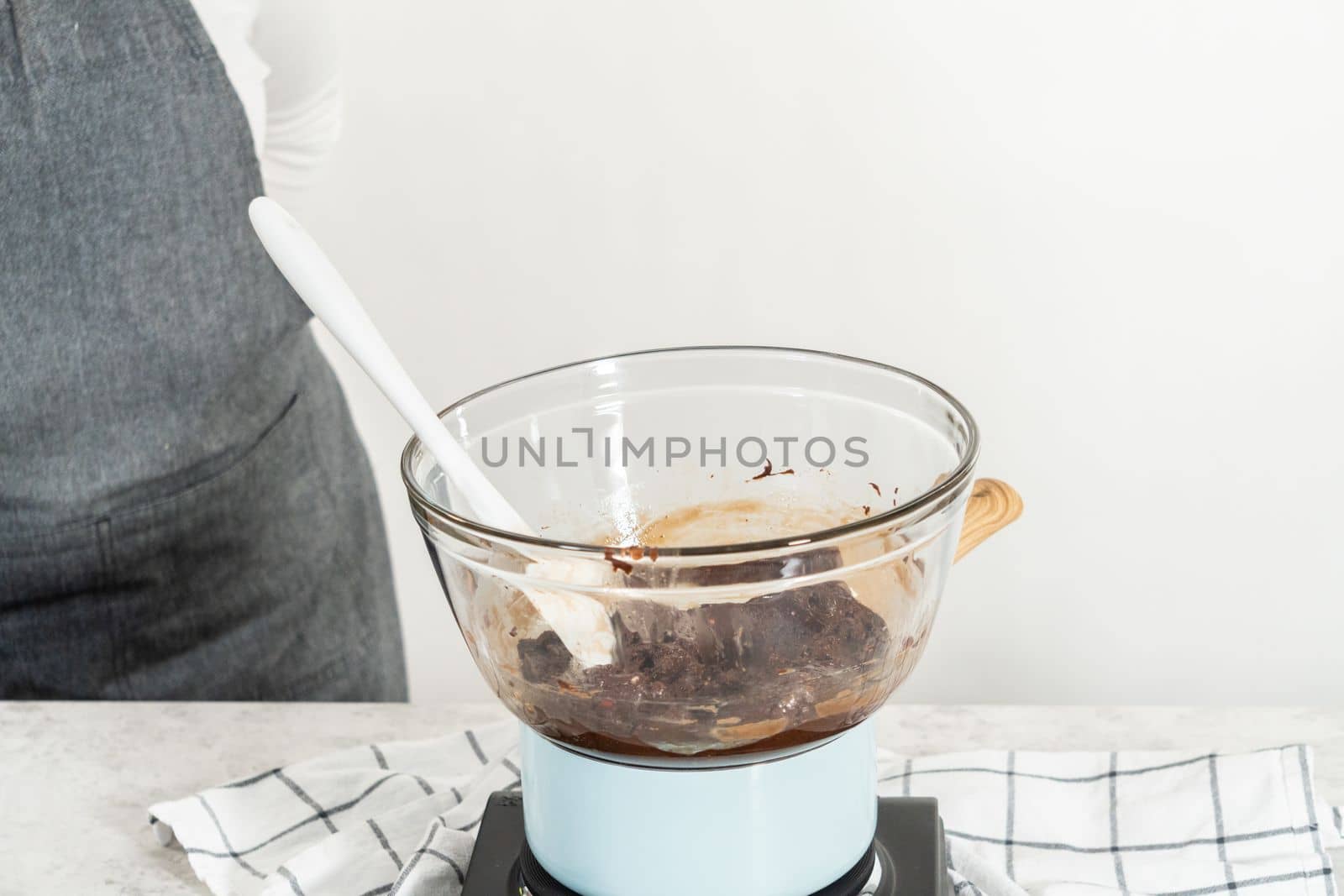 Melting white chocolate chips and other ingredients in a glass mixing bowl over boiling water to prepare candy cane fudge.