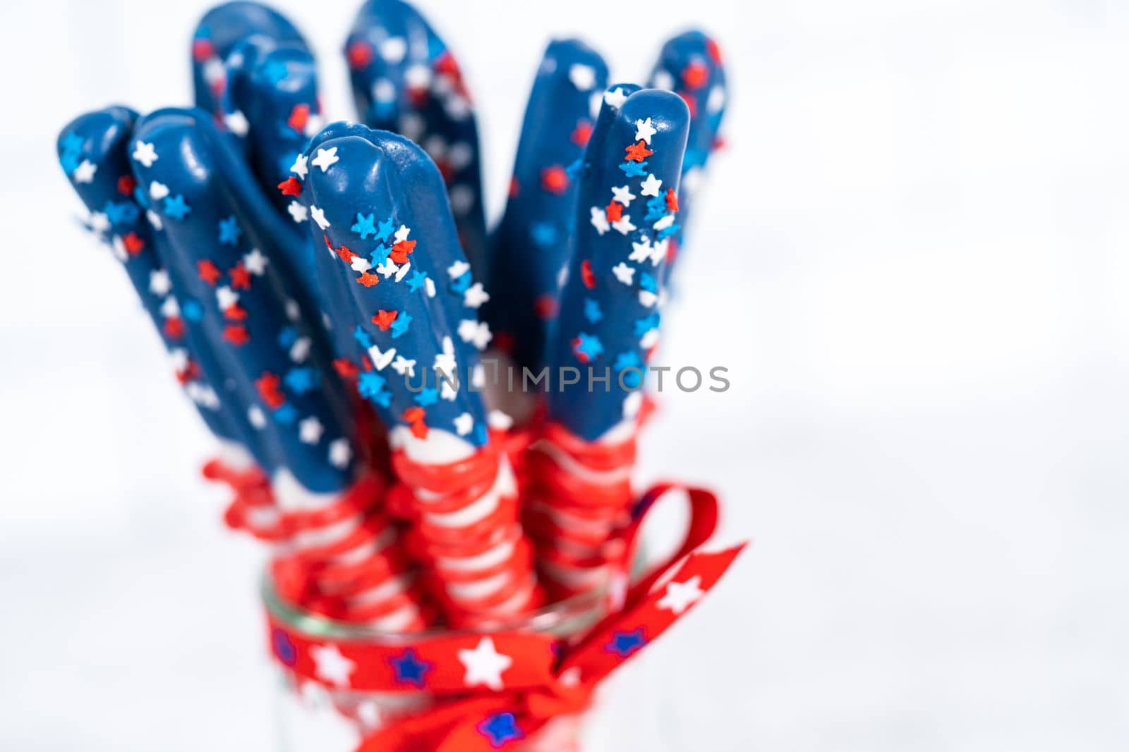 Homemade chocolate-covered pretzel rods decorated like the American flag in a glass jar.