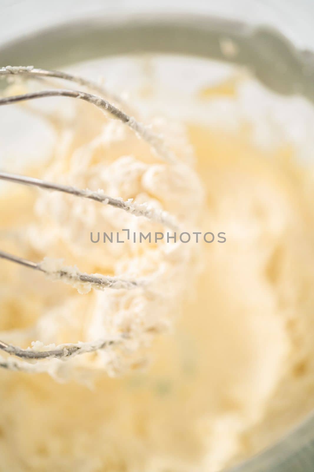 Mixing ingredients in a large glass mixing bowl of kitchen mixer to make eggnog buttercream frosting.