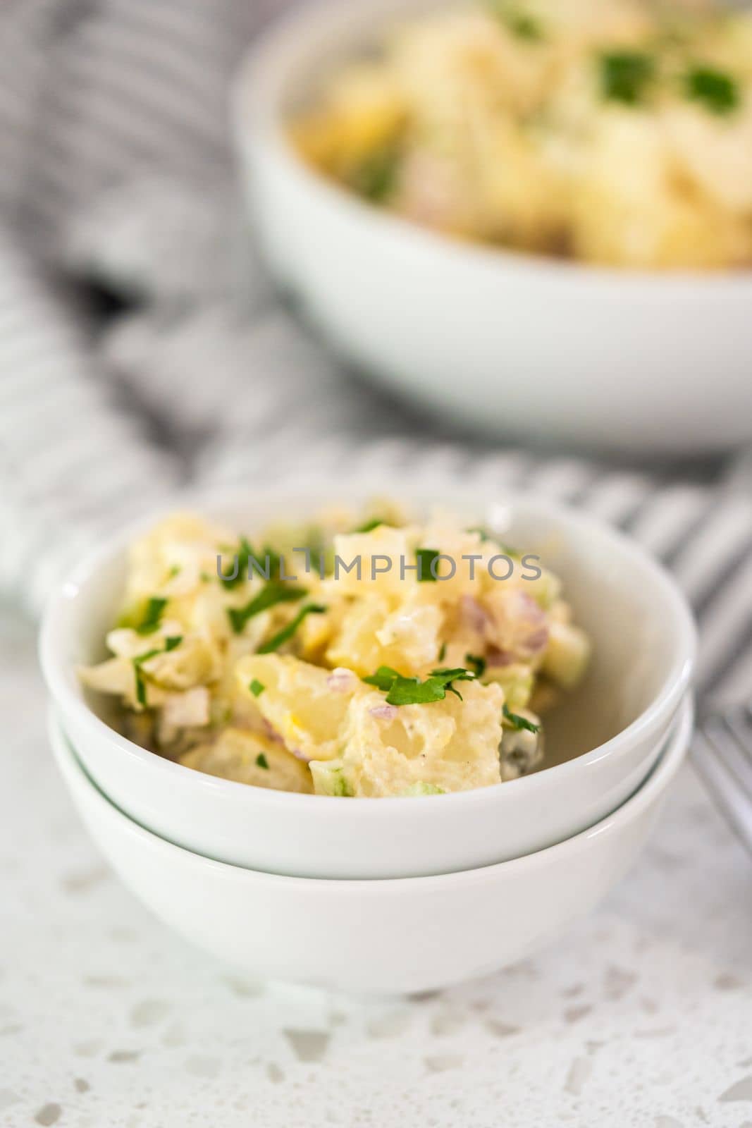 Serving potato salad garnished with fresh parsley in a white ceramic bowl.