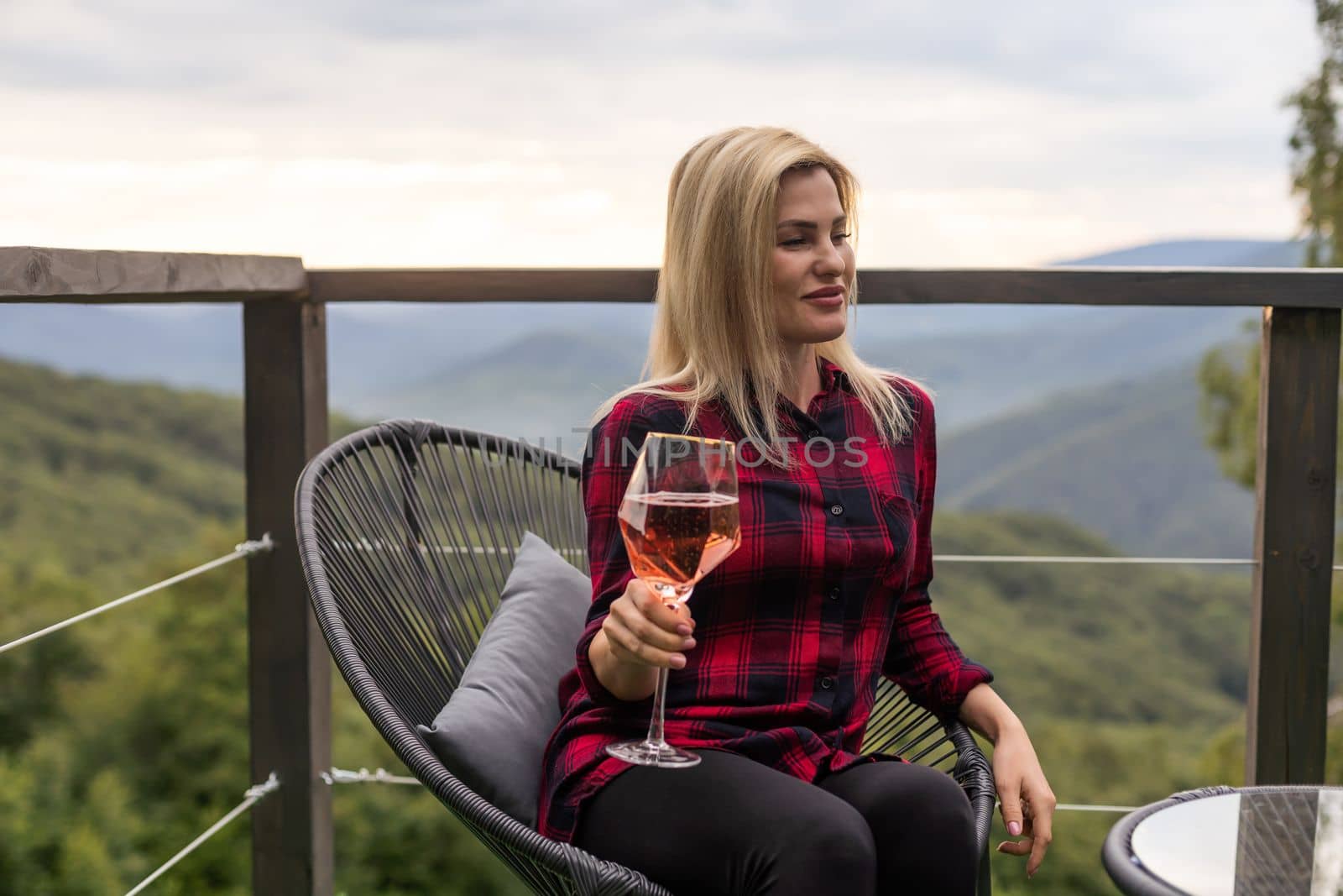 Woman holding glass of white wine across beautiful mountains landscape and sunset.