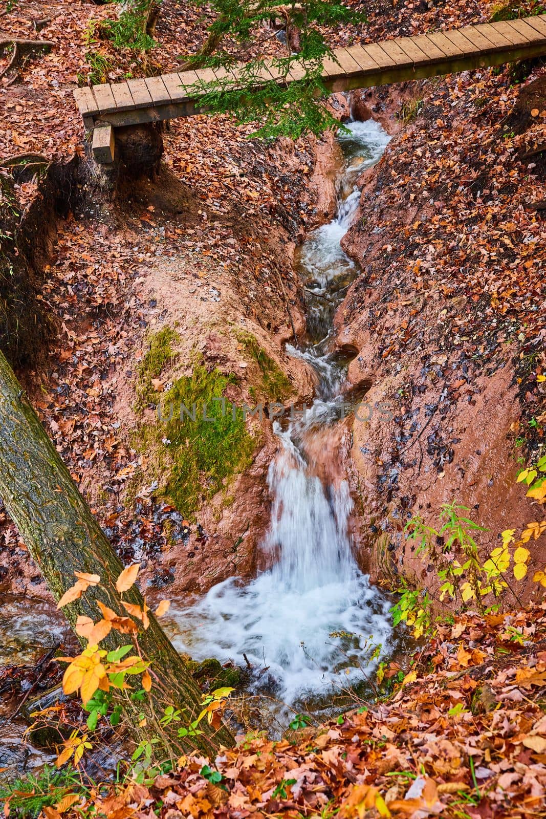 Image of Clay carved river creek with waterfall and walking bridge in fall forest