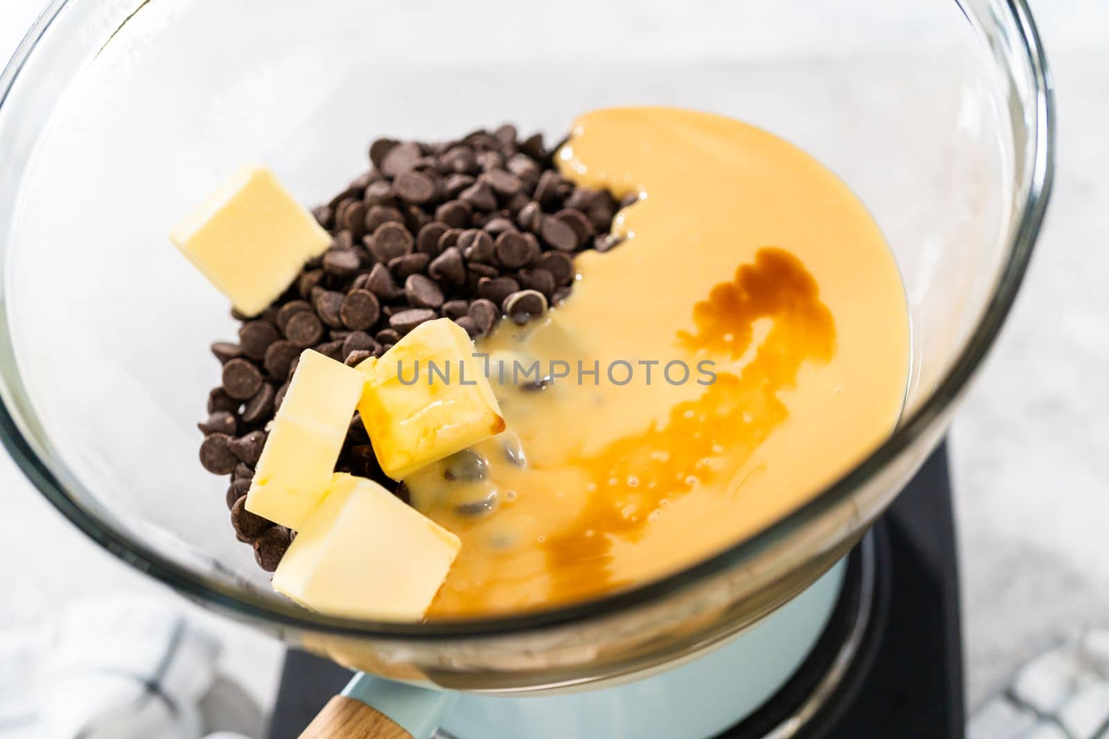Melting white chocolate chips and other ingredients in a glass mixing bowl over boiling water to prepare chocolate macadamia fudge.