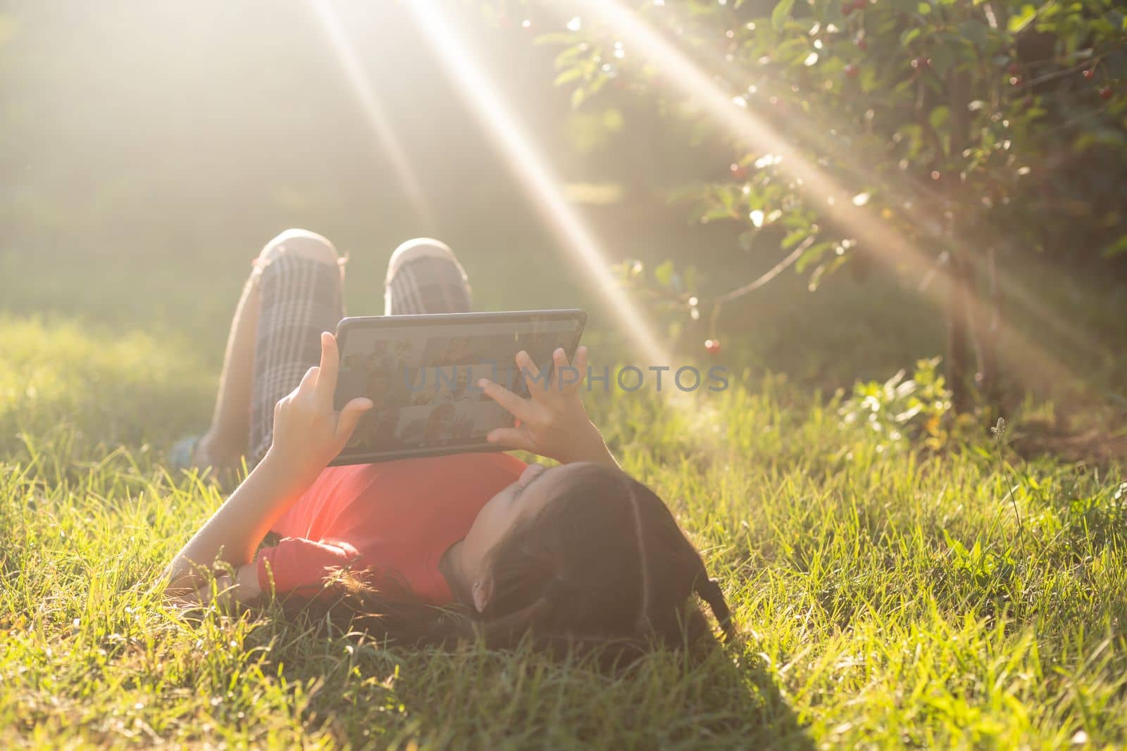 Child girl playing on a Digital tablet in the garden. Online or Remote education concept.