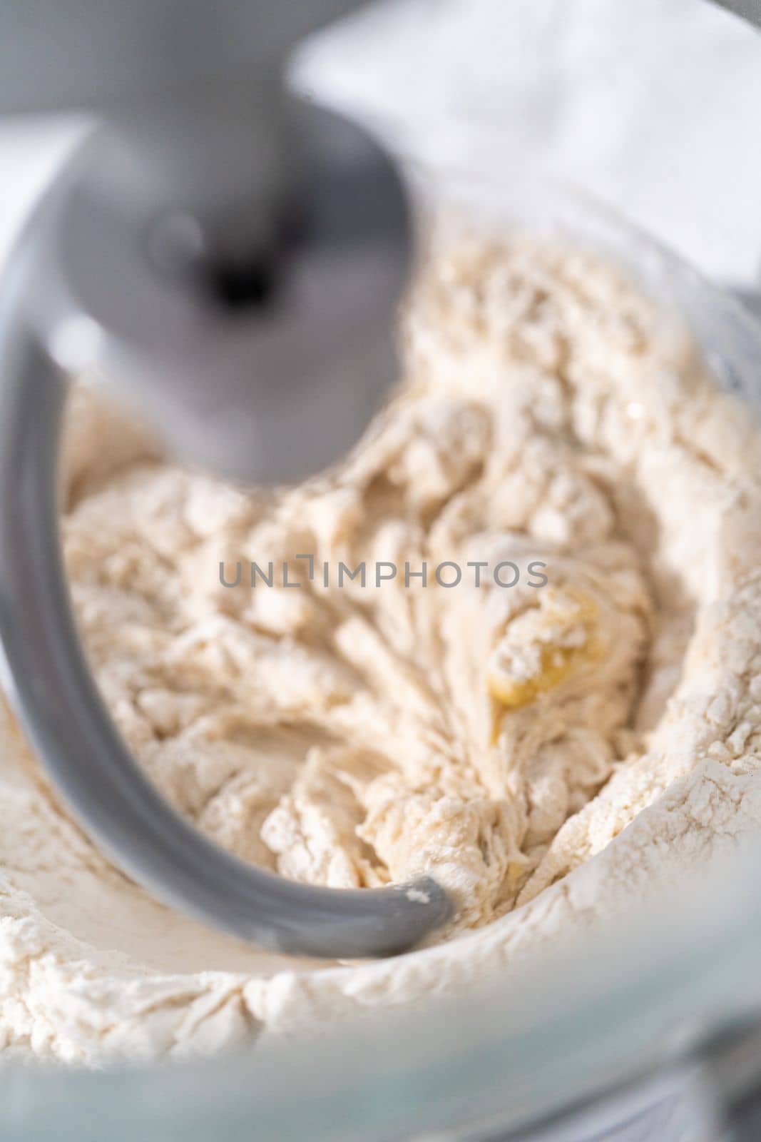 Mixing ingredients in a large glass mixing bowl to pizza dough.