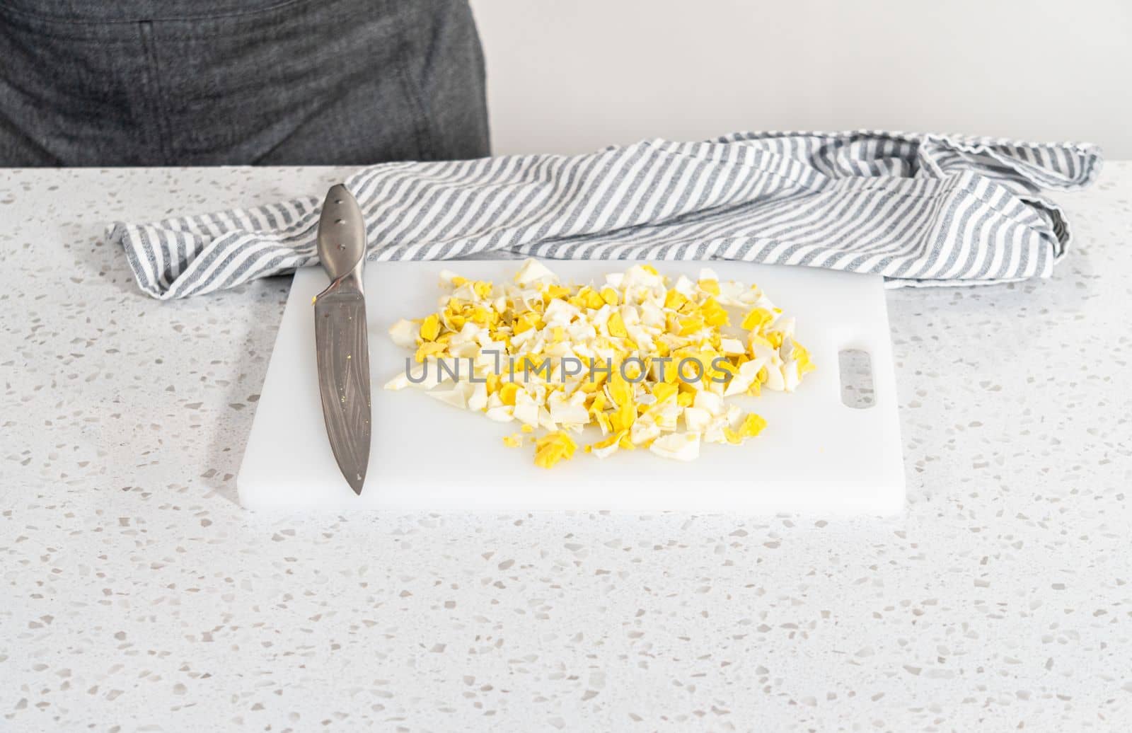 Cutting hard-boiled eggs on a white cutting board to make potato salad.