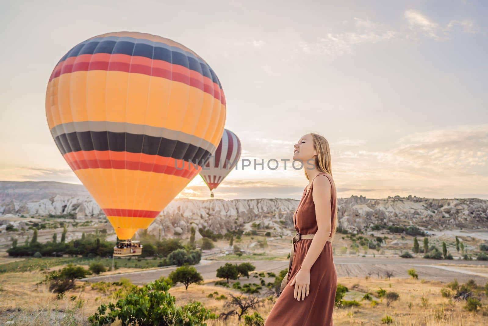 Tourist woman looking at hot air balloons in Cappadocia, Turkey. Happy Travel in Turkey concept. Woman on a mountain top enjoying wonderful view.