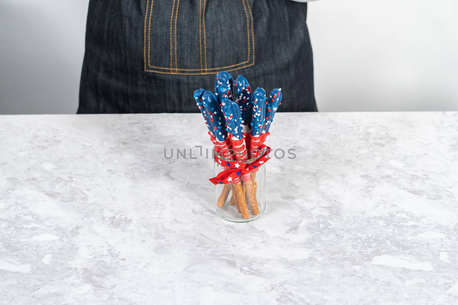 Homemade chocolate-covered pretzel rods decorated like the American flag in a glass jar.