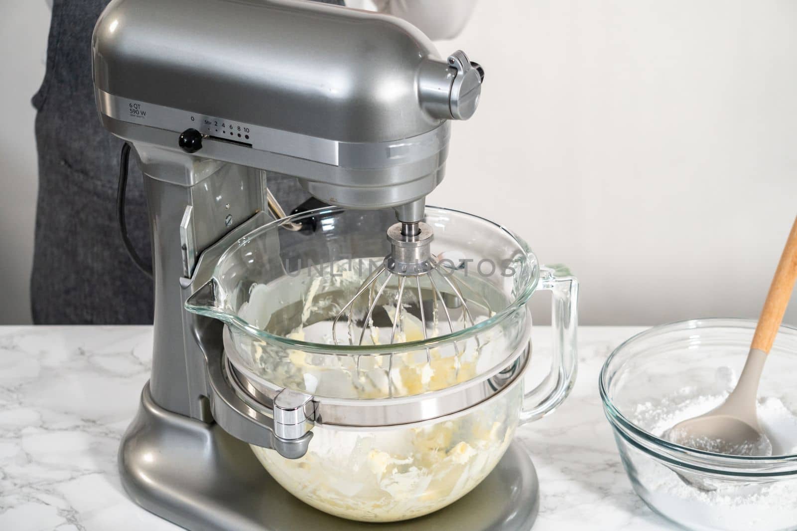 Mixing ingredients in a large glass mixing bowl of kitchen mixer to make eggnog buttercream frosting.