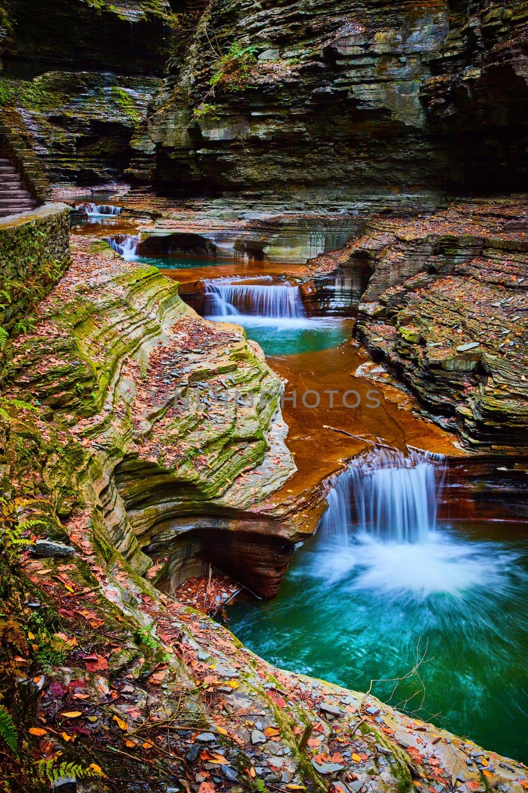 Image of River with cascading buckets of blue water and waterfalls through gorge of terraced rocks covered in fall leaves