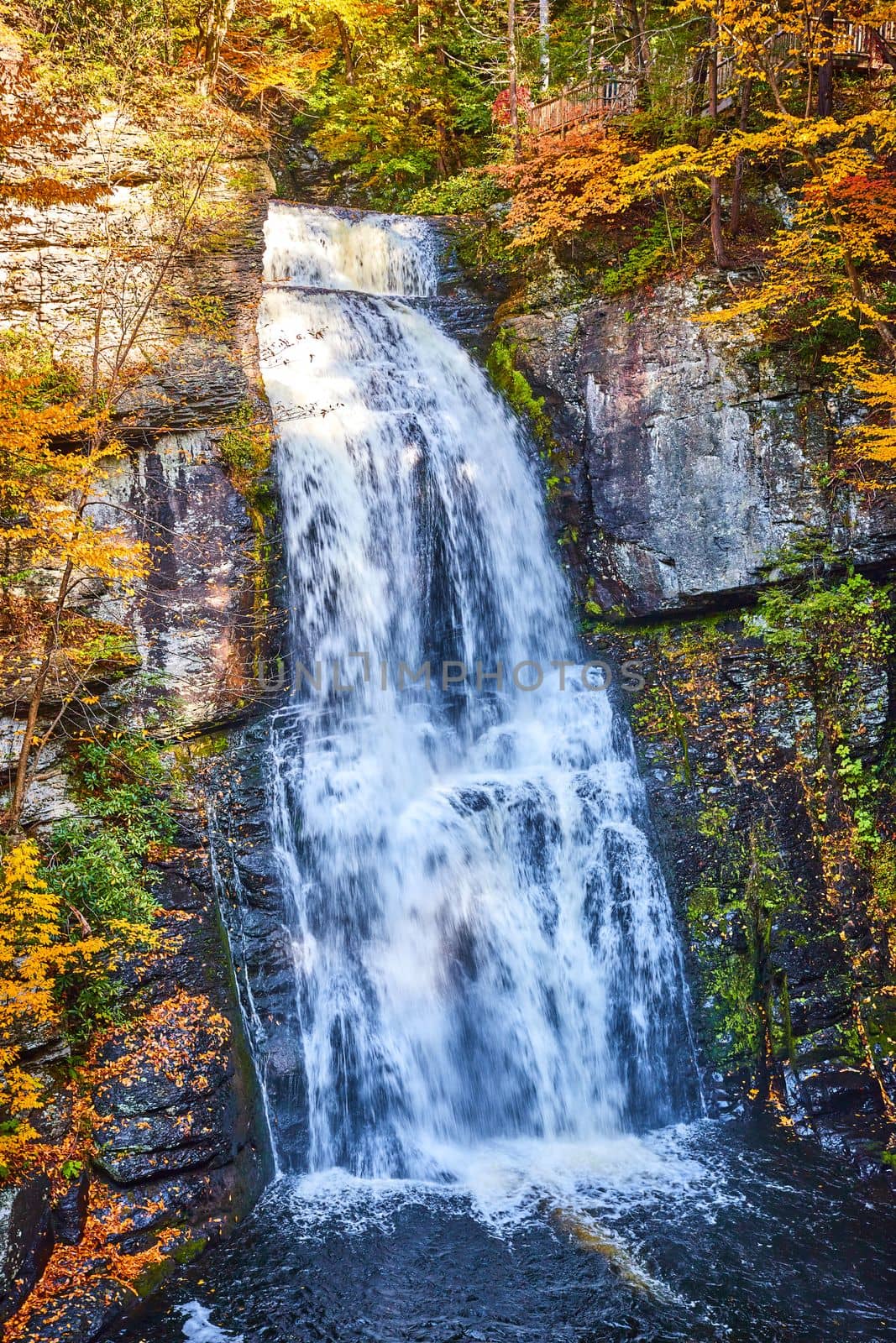 Image of Straight on huge waterfall over cliffs with harsh light and fall foliage around