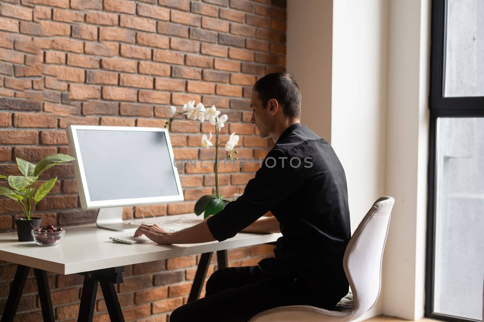 Focused young man using laptop, typing on keyboard, writing email or message, chatting, shopping, successful freelancer working online on computer