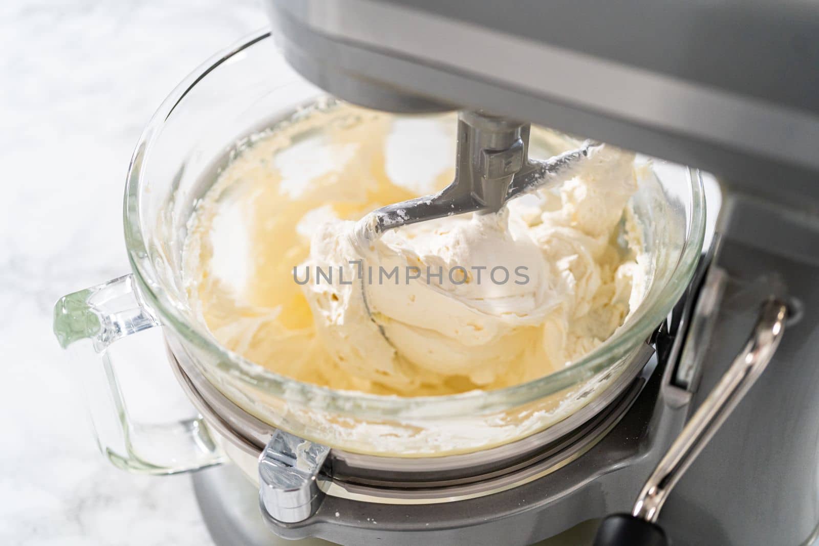 Whisking buttercream frosting in a glass mixing bowl with an electric kitchen mixer for American flag mini cupcakes.