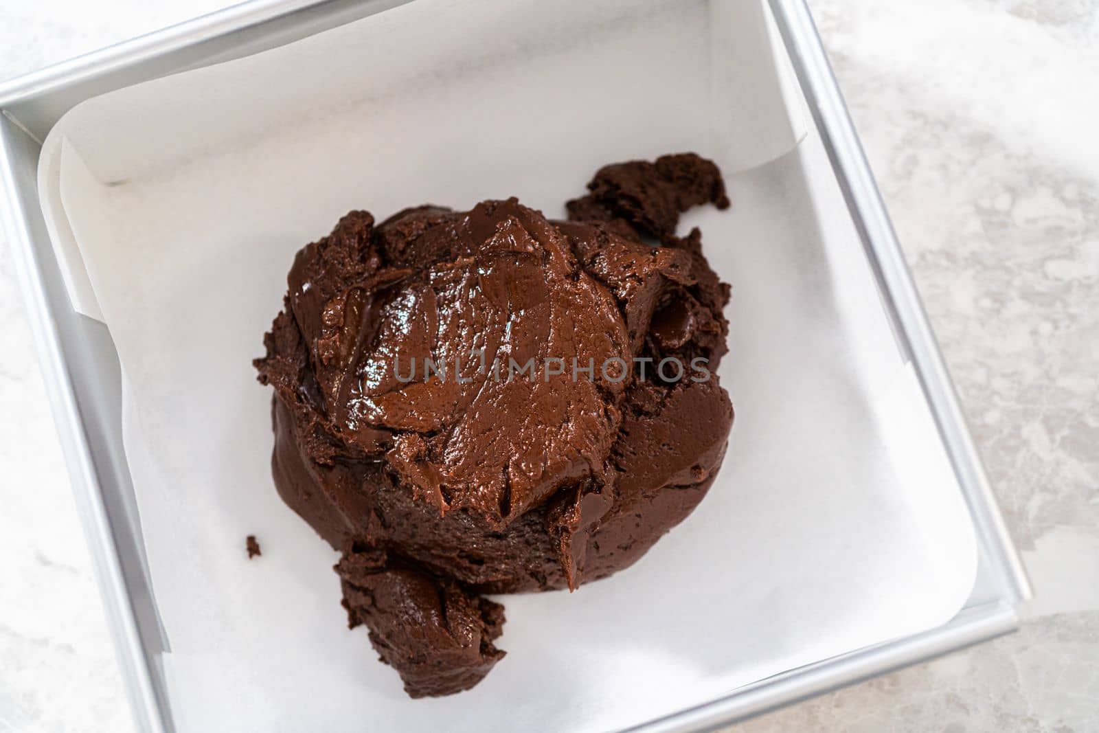Filling square cheesecake pan lined with parchment paper with fudge mixture to prepare candy cane fudge.