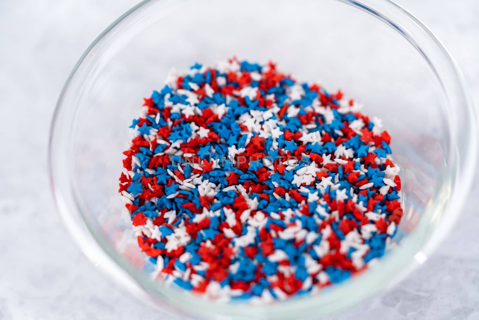 Star-shaped white, red, and blue sprinkles in a glass pinch bowl.