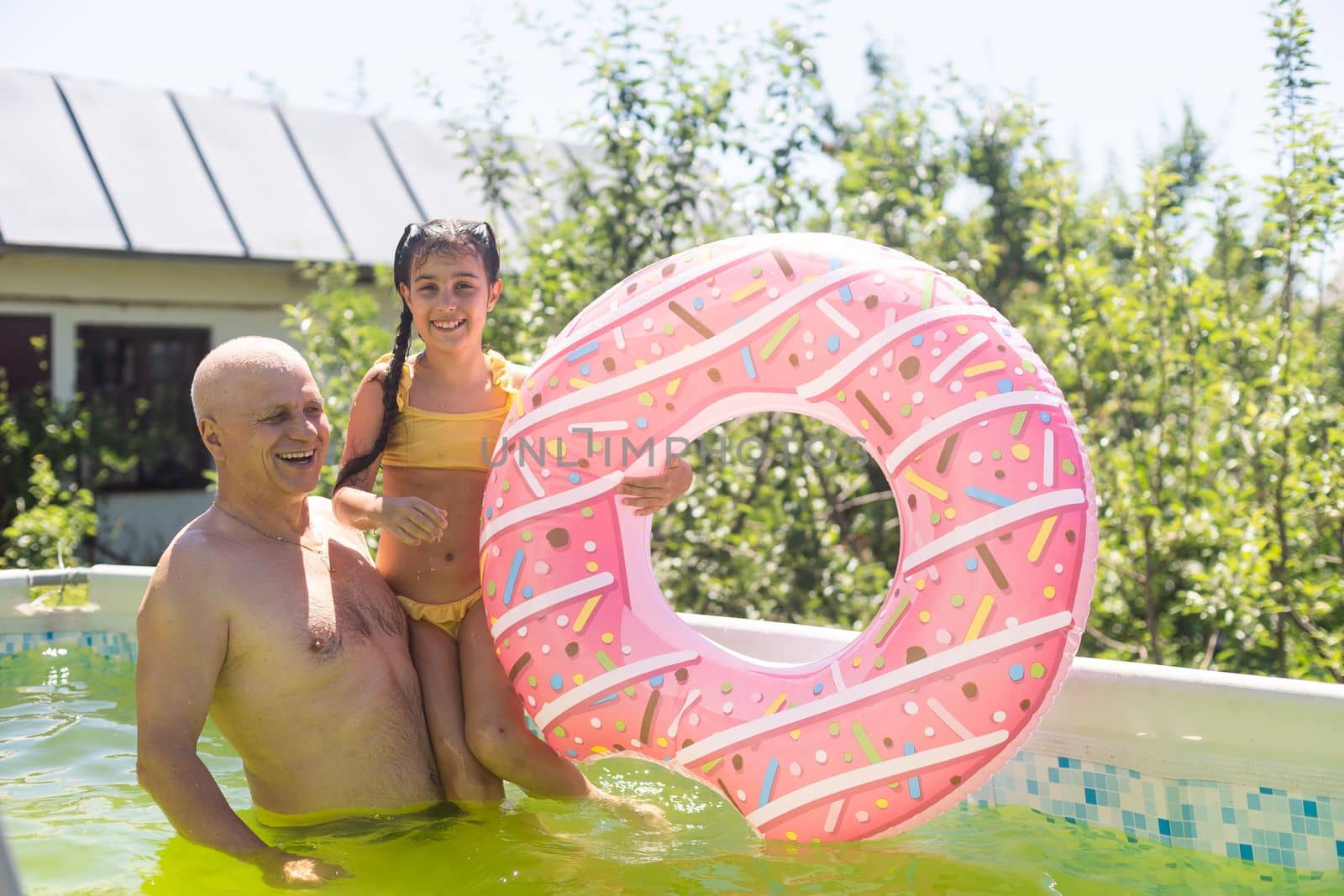 grandfather and granddaughter swimming in the pool in the garden near the house by Andelov13