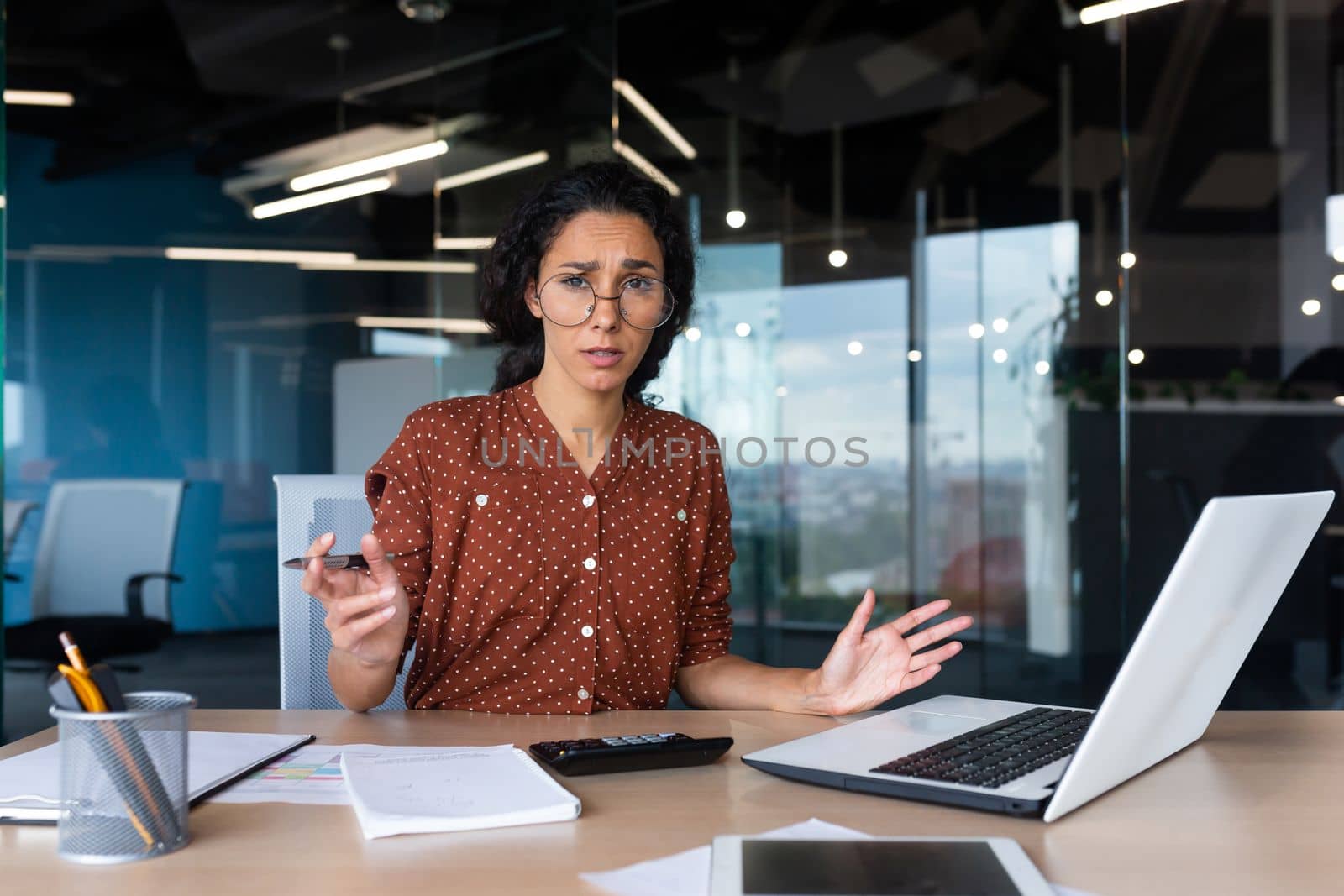 Frustrated and tired business woman looking at camera, Hispanic woman unhappy with work result, working inside office using laptop at work.