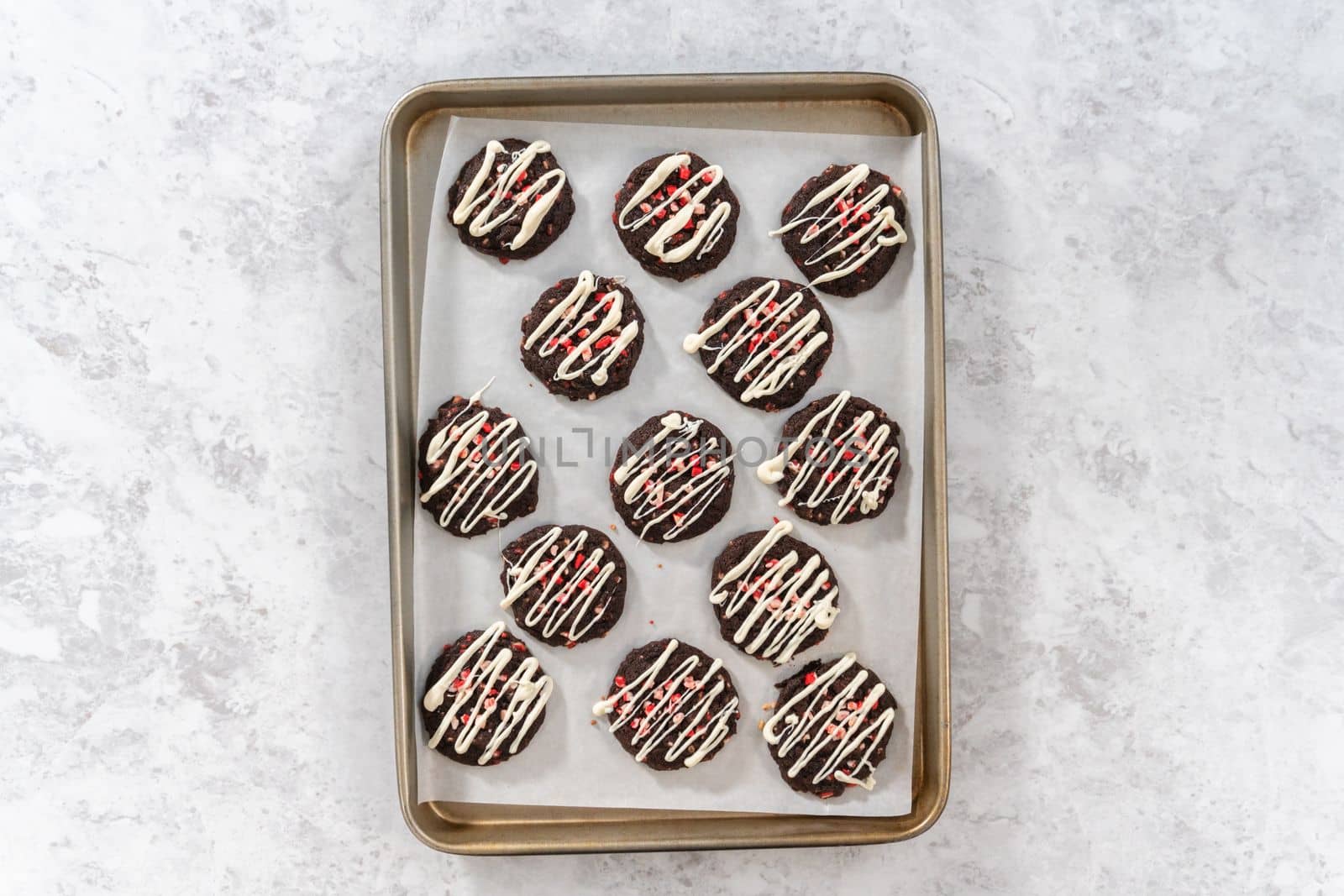 Flat lay. Drizzling melted white chocolate over freshly baked chocolate cookies with peppermint chips.