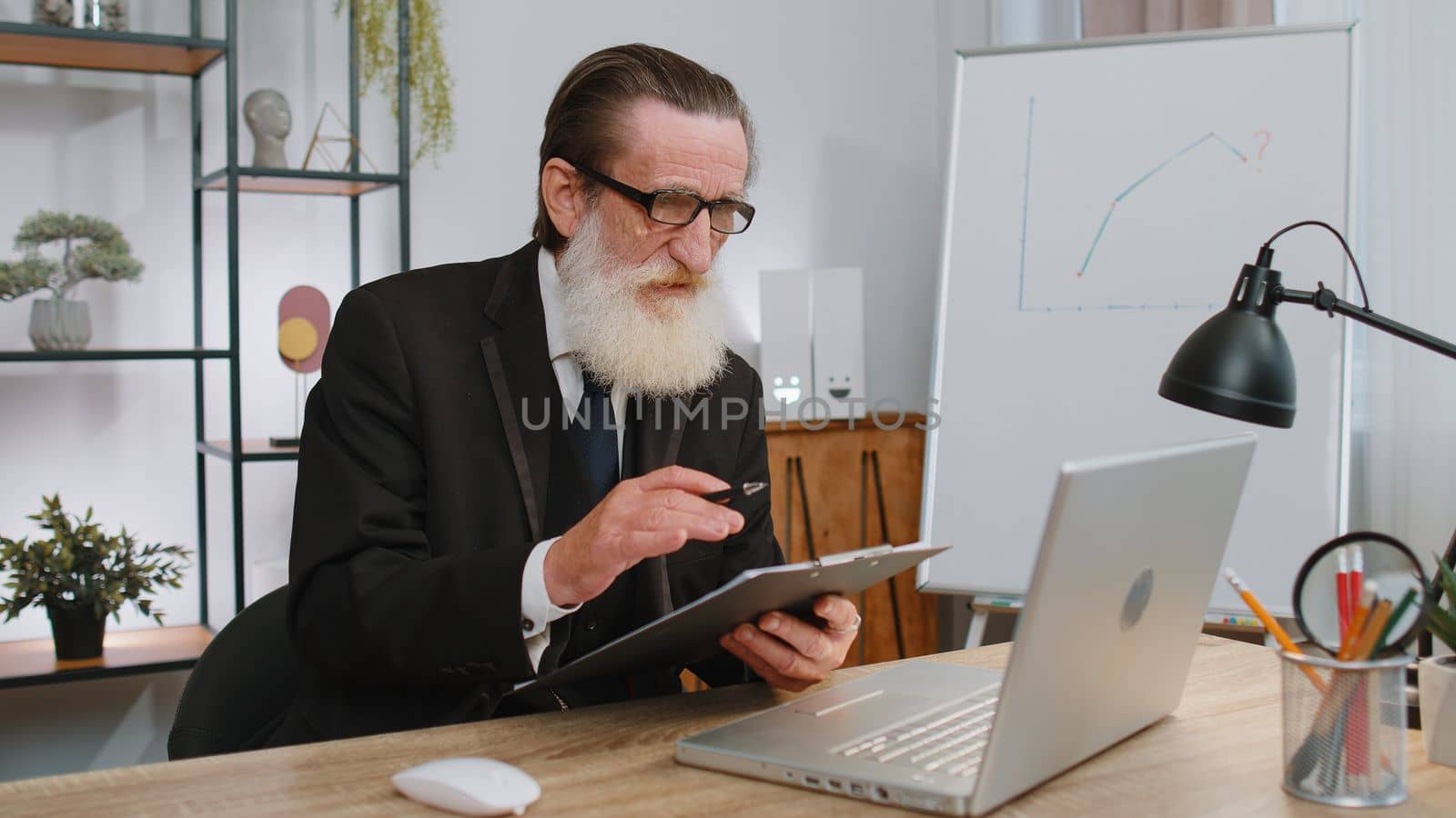Senior businessman working on laptop computer at home office desk talk on online communication video call with employee, boss. Manager grandfather old man freelancer support services looking at camera
