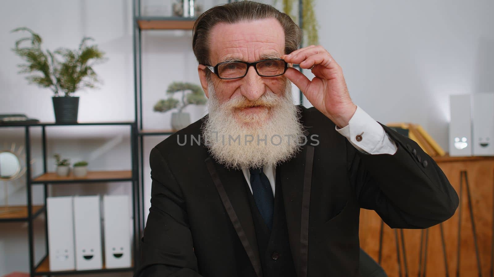 Confident happy senior businessman in glasses looking at camera with smile at home office desk workplace. Face portrait of elderly grandfather freelancer worker entrepreneur, company leader boss man