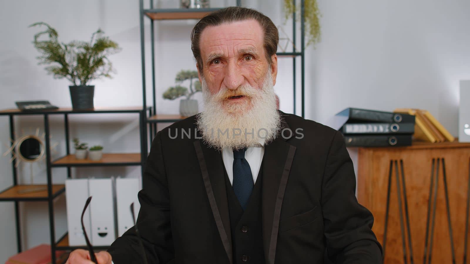 Confident happy senior businessman taking off glasses looking at camera with smile at home office workplace. Face portrait of elderly grandfather freelancer director, worker, company leader boss man