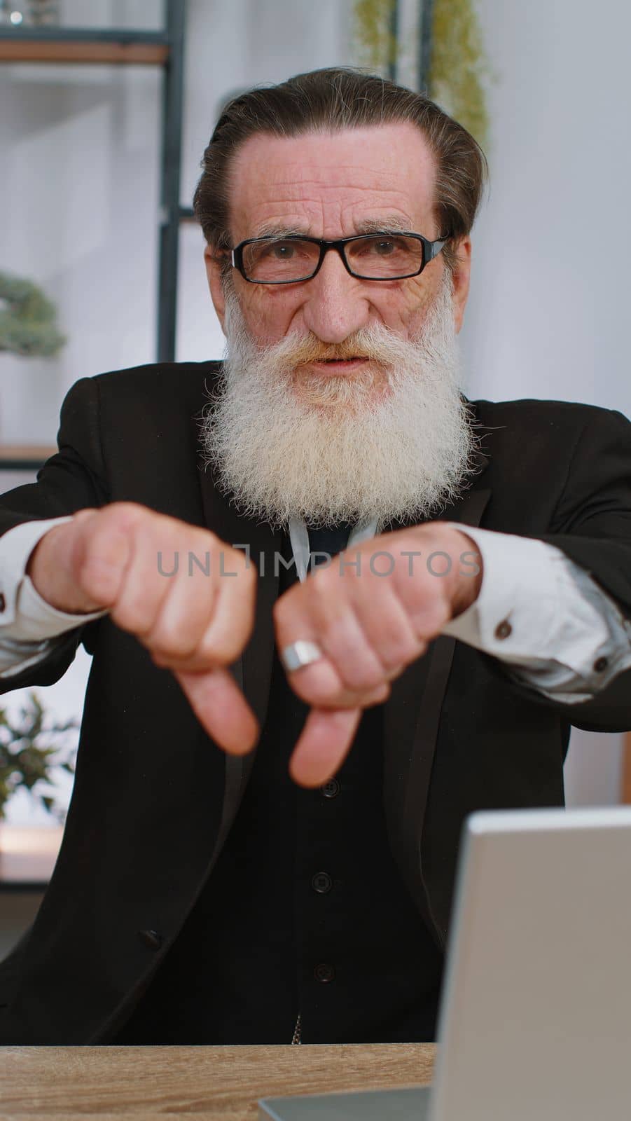 Dislike. Upset senior businessman working on laptop computer at home office thumbs down sign gesture, expressing discontent, disapproval, dissatisfied bad work. Displeased serious freelancer old man