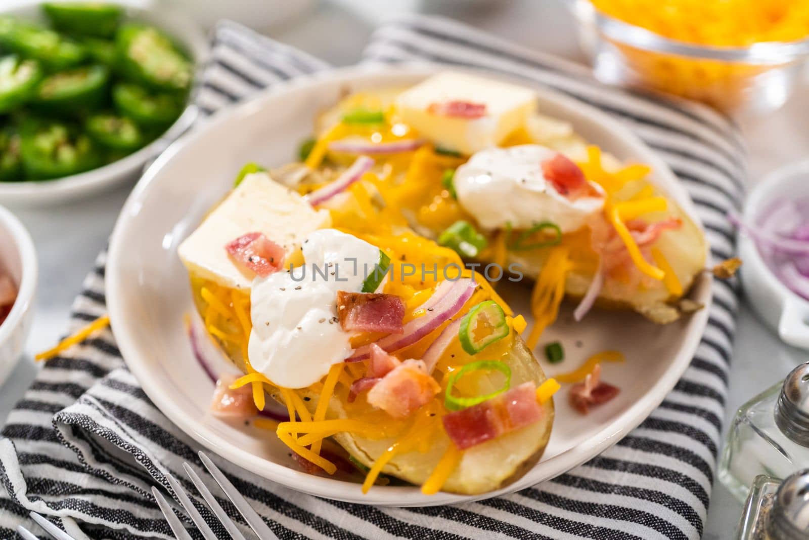 Pressure Cooker Baked Potatoes. Garnished large baked potatoes with butter, sour cream, cheese, and bacon bits on a white plate.