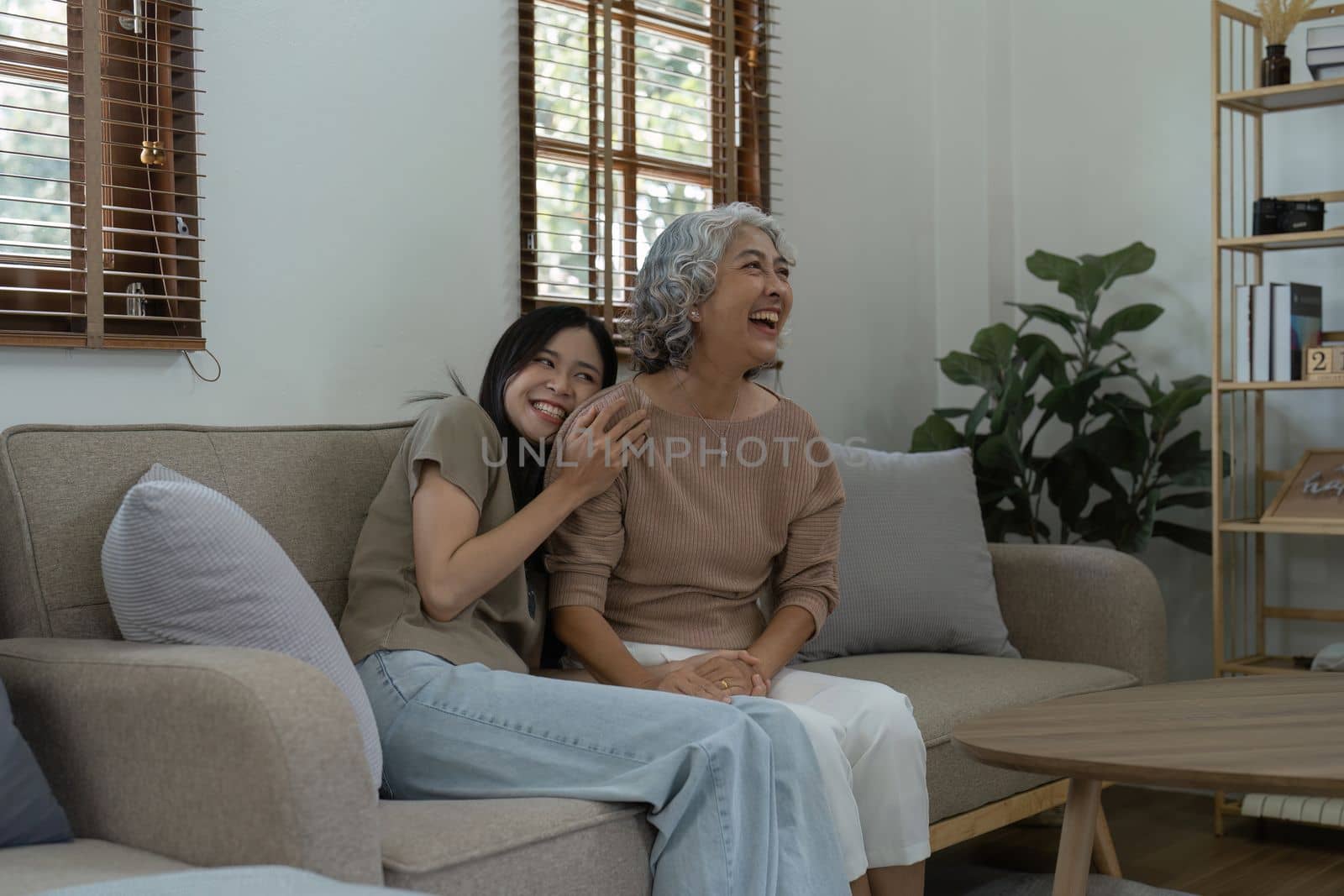 Loving adult daughter hugging older mother on couch at home, family enjoying tender moment together, young woman and mature mum or grandmother looking at each other, two generations by itchaznong