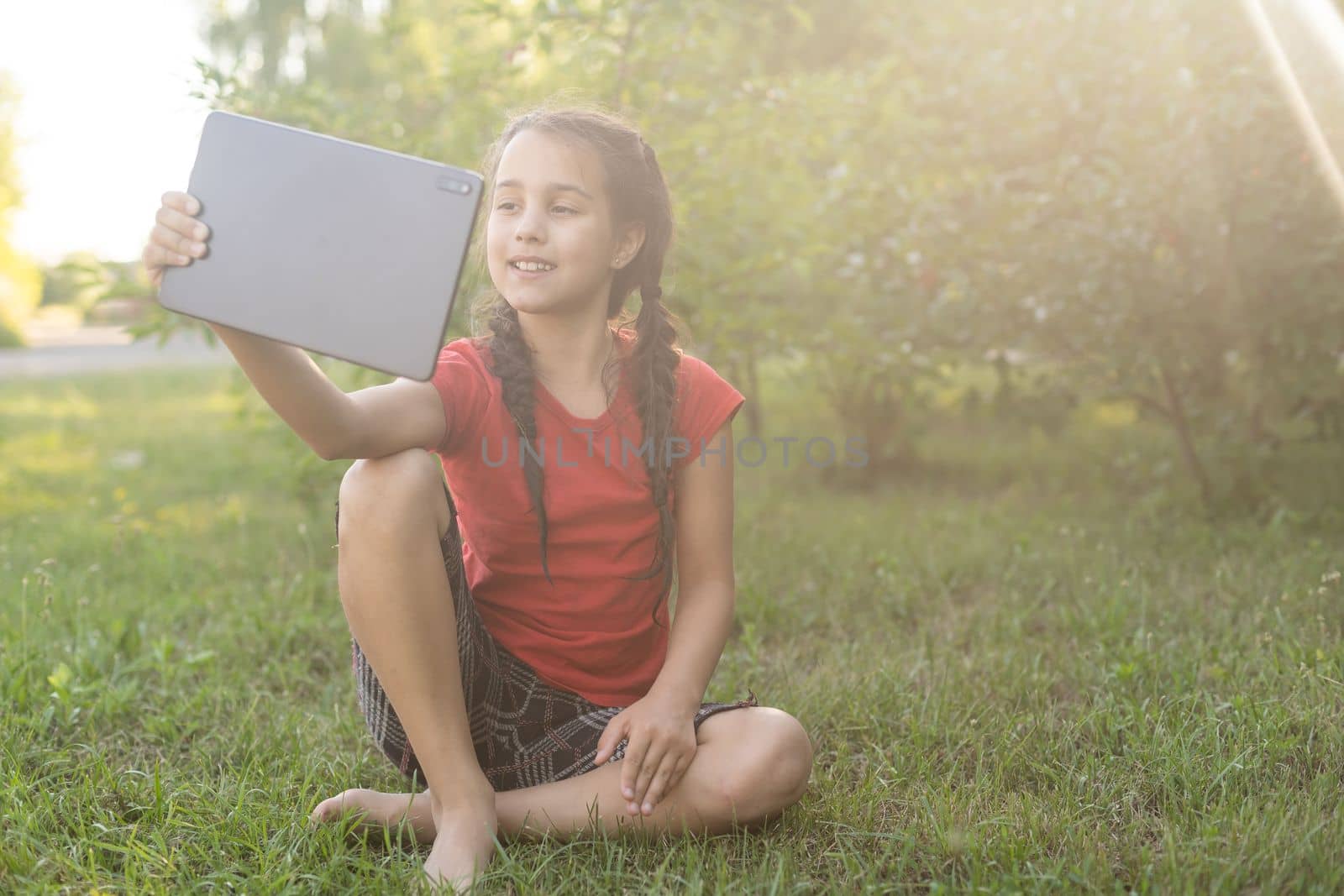 Child girl playing on a Digital tablet in the garden. Online or Remote education concept.