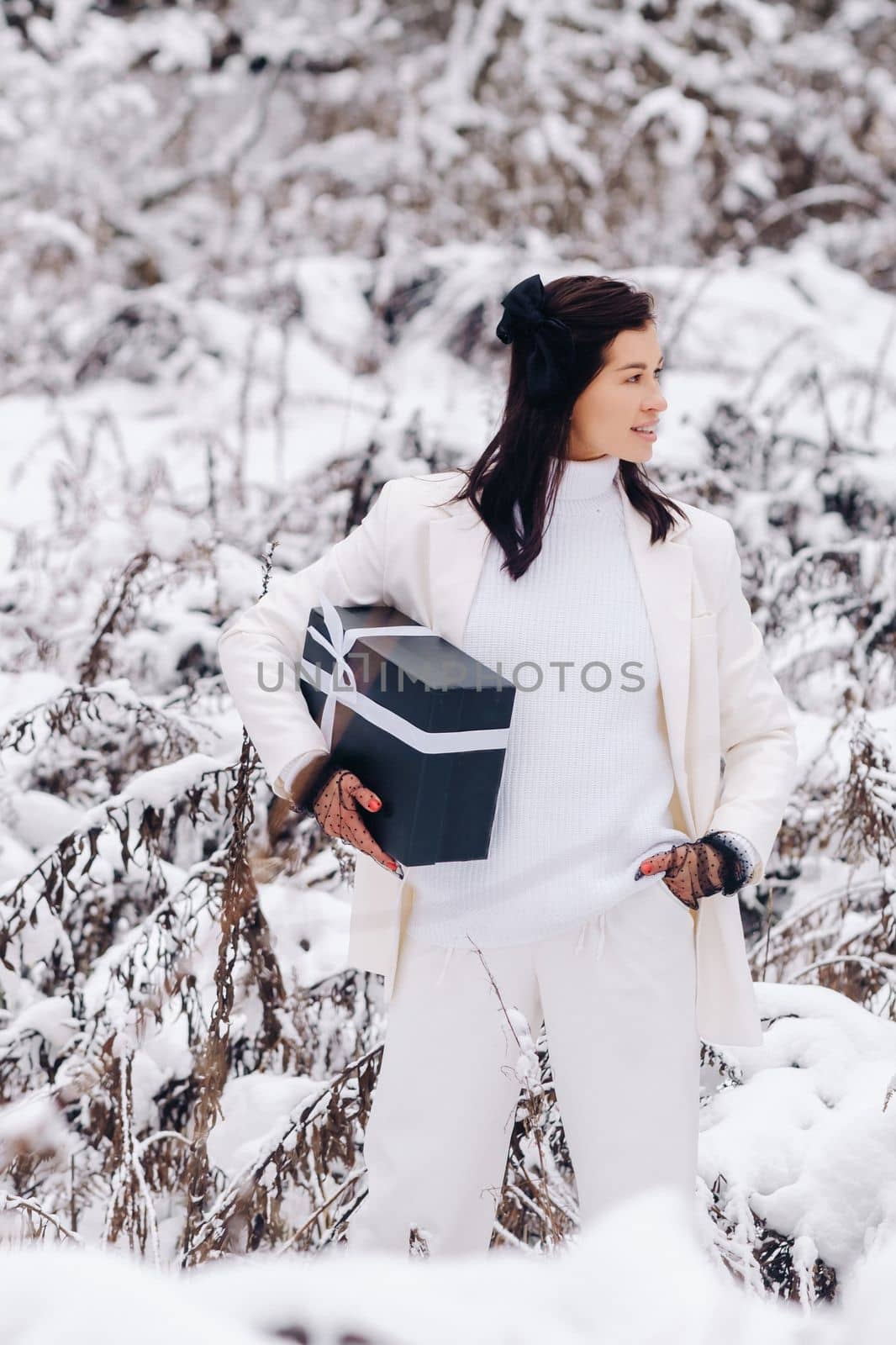 A stylish woman with a white suit with a New Year's gift in her hands in a winter forest. A girl in nature in a snowy forest with a gift box by Lobachad