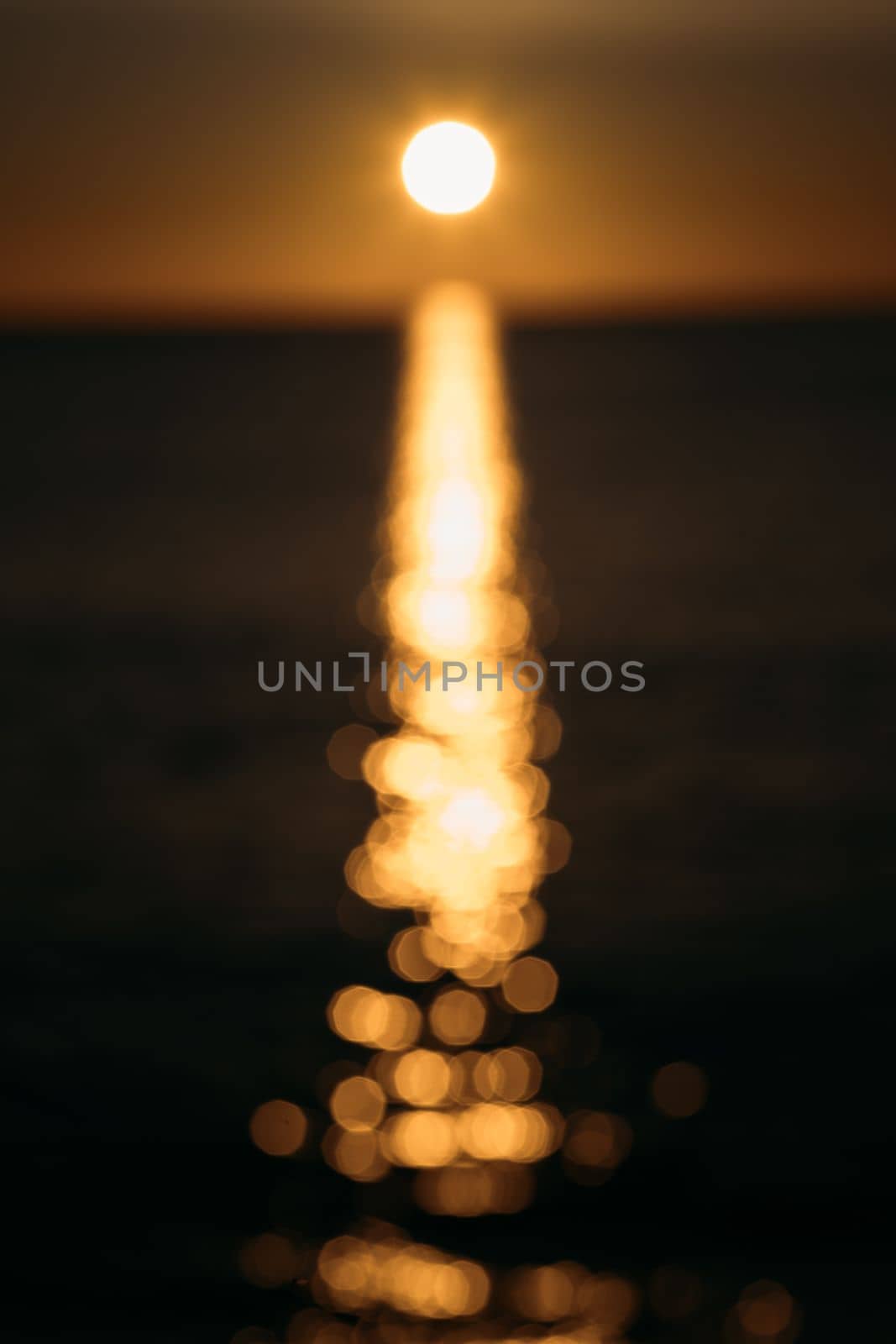 On a blurry abstract blurred sunset background, a bright yellow sun disk casts glare on the sea water. Gorgeous golden blurred sunset background in the coming dusk of the tropics