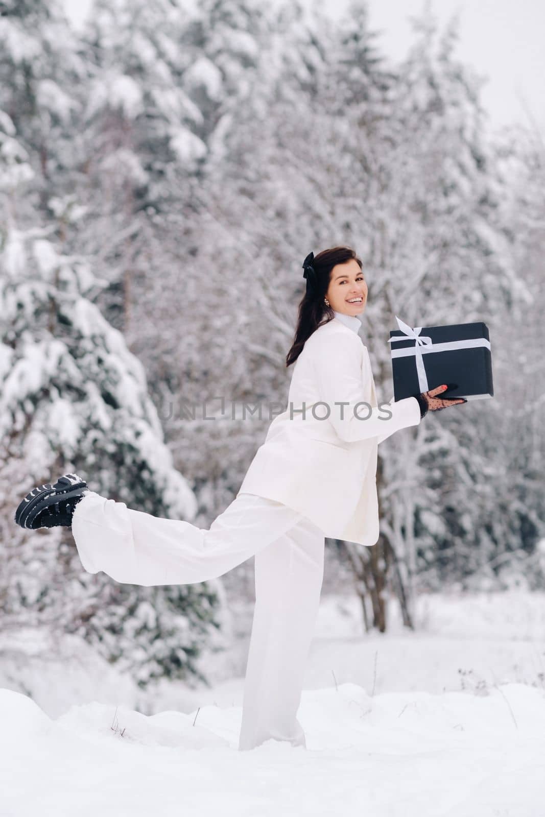 A stylish woman with a white suit with a New Year's gift in her hands in a winter forest. A girl in nature in a snowy forest with a gift box by Lobachad