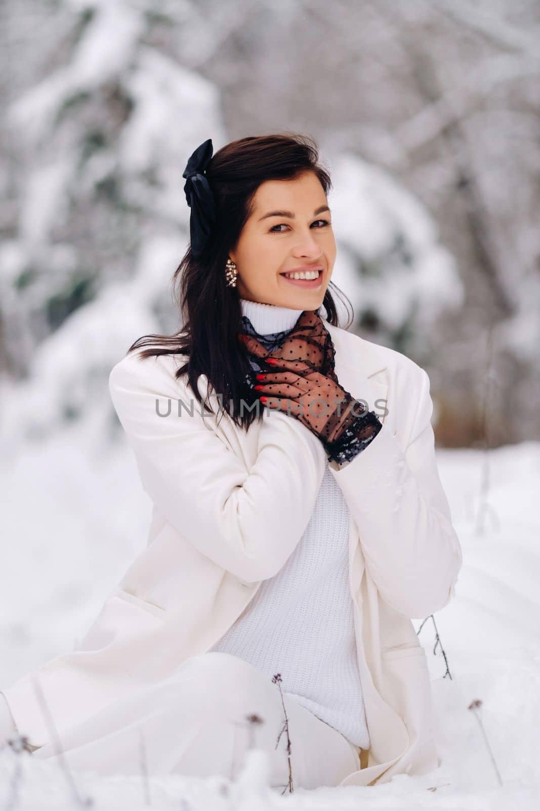 Portrait of a stylish woman in a white suit with elegant gloves sitting in nature in winter by Lobachad