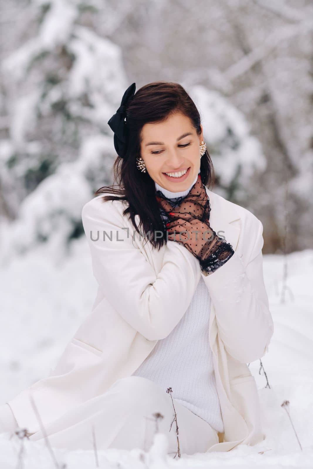 Portrait of a stylish woman in a white suit with elegant gloves sitting in nature in winter.
