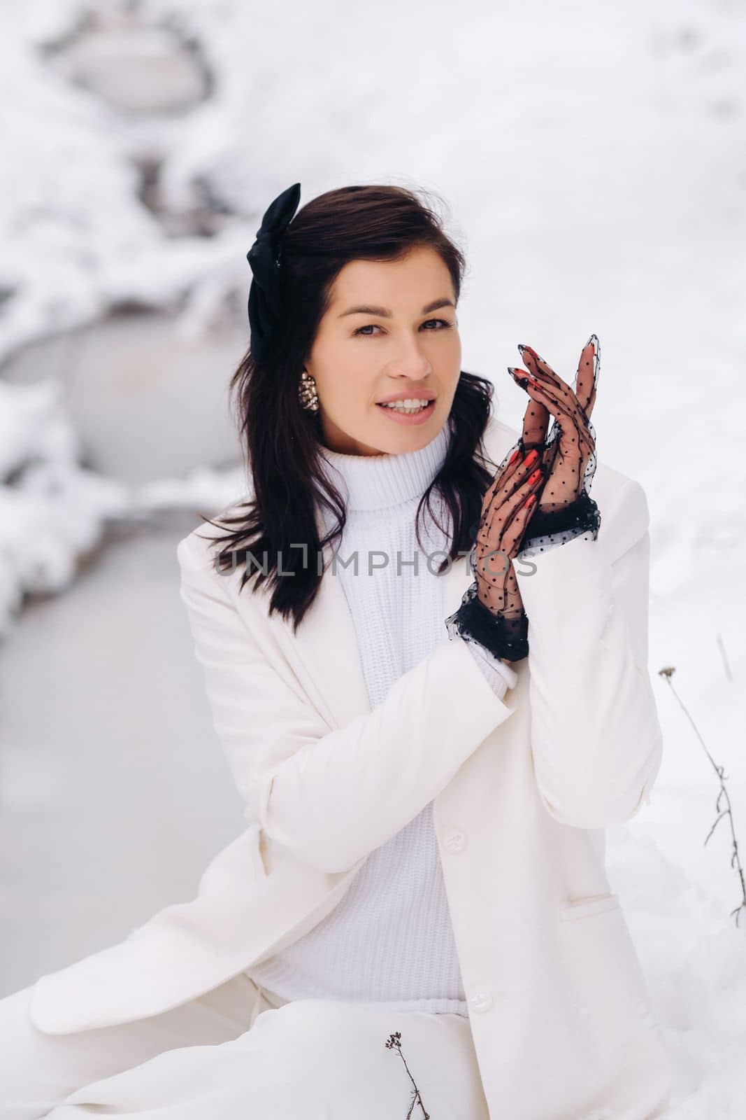 Portrait of a stylish woman in a white suit with elegant gloves sitting in nature in winter by Lobachad